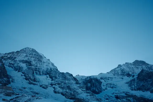 Snow-covered alpine peaks against a clear deep blue sky at dusk