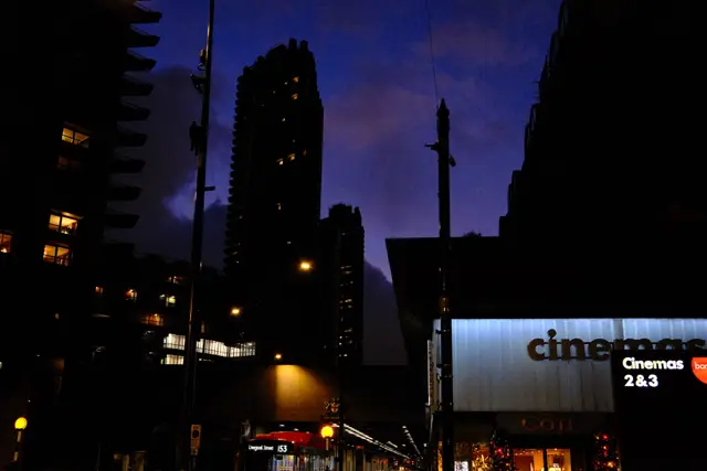 A cinema sign illuminated at night with city tower blocks against a deep blue sky