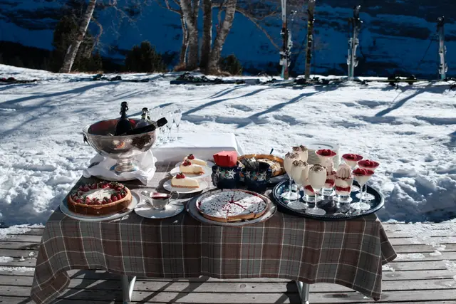 An outdoor dessert table laid with cakes and puddings in a snowy alpine setting