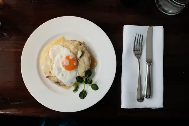 A fried egg on polenta on a white plate, cutlery and a white napkin alongside