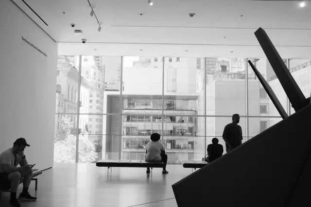 Black-and-white view of a MoMA gallery with figures on benches looking out over the city