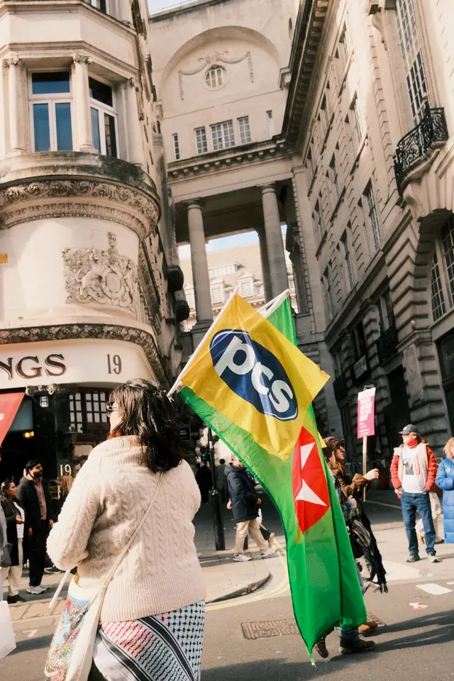 A protester carrying a yellow PCS union flag past grand stone buildings on Air Street in central London