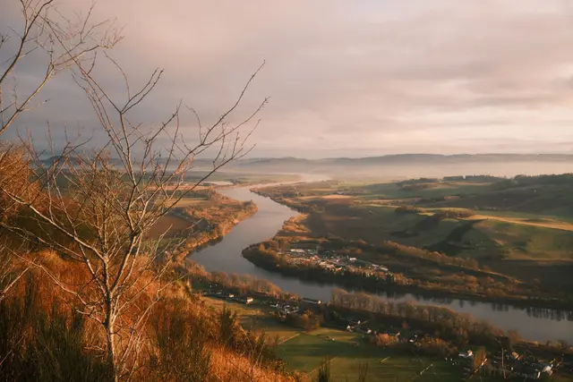 A winding river through a golden valley at sunrise, mist over distant hills