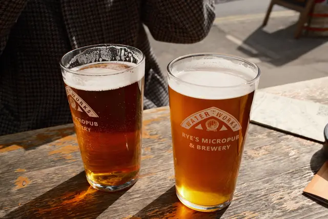 Two pints of ale on a wooden table outside Rye's Micropub & Brewery, lit by bright afternoon sun