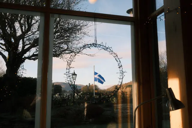 View through a window with a Shetland flag outside, hills and bare trees in the background